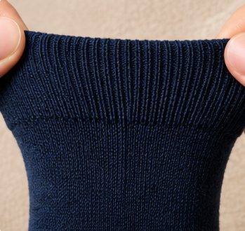 Macro close-up of the soft ribbed non-binding cuff of a navy Kilde mercerized cotton sock gently stretched between a thumb and index finger on beige linen